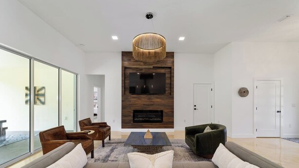 Un salon moderne avec un grand canapé, deux fauteuils, une table basse, une cheminée et un téléviseur fixé à un mur en bois.
