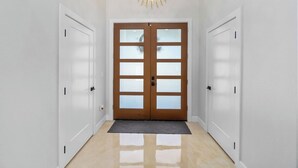 Un couloir avec une porte à deux battants, un luminaire et un paillasson.