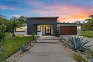 A modern two-story house with a garage, a front entrance with a glass door, and a well-maintained garden with agave plants.