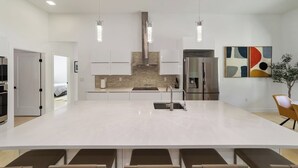 Une cuisine moderne dotée d’un grand îlot central, d’appareils électroménagers en acier inoxydable, de luminaires suspendus et d’œuvres d’art abstraites accrochées au mur.