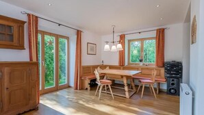 Une cuisine spacieuse avec des meubles en bois, une table à manger avec des chaises, de grandes fenêtres avec des rideaux et un radiateur.
