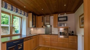 Une cuisine avec des meubles en bois, un four à micro-ondes, un four traditionnel et une fenêtre donnant sur un paysage verdoyant.