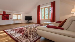Un salon spacieux avec une table basse en verre, un canapé beige agrémenté de coussins rouges, un téléviseur à écran plat et une grande fenêtre ornée de rideaux rouges.