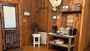 Un intérieur rustique avec des murs en bois, un grand tapis en cuir marron, un coin café et un panneau encadré sur lequel on peut lire : « Né pour la chasse ».