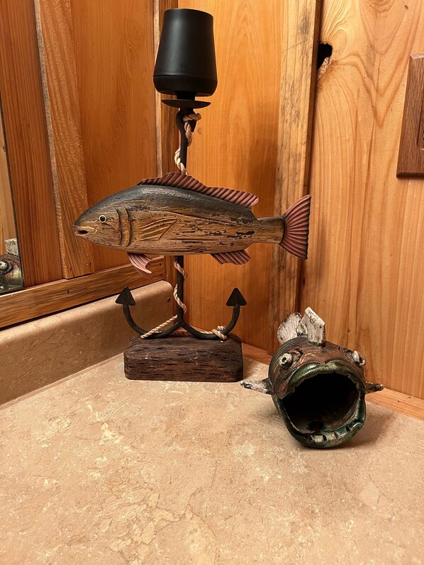 Una escultura de madera con forma de pez, con una lámpara en la parte superior, una cuerda y una cabeza de pez sobre un pedestal.