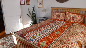 Une chambre à coucher avec un lit en bois, une literie à motifs, une table de chevet, une lampe et une plante en pot.