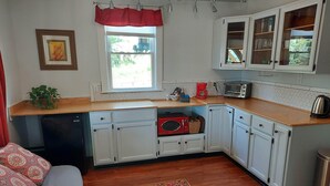 Une cuisine de taille réduite avec des meubles blancs, un four à micro-ondes, un grille-pain et une machine à café rouge.