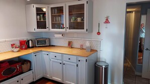 Une cuisine avec des meubles blancs, un plan de travail en bois, une machine à café rouge, un grille-pain et une poubelle.