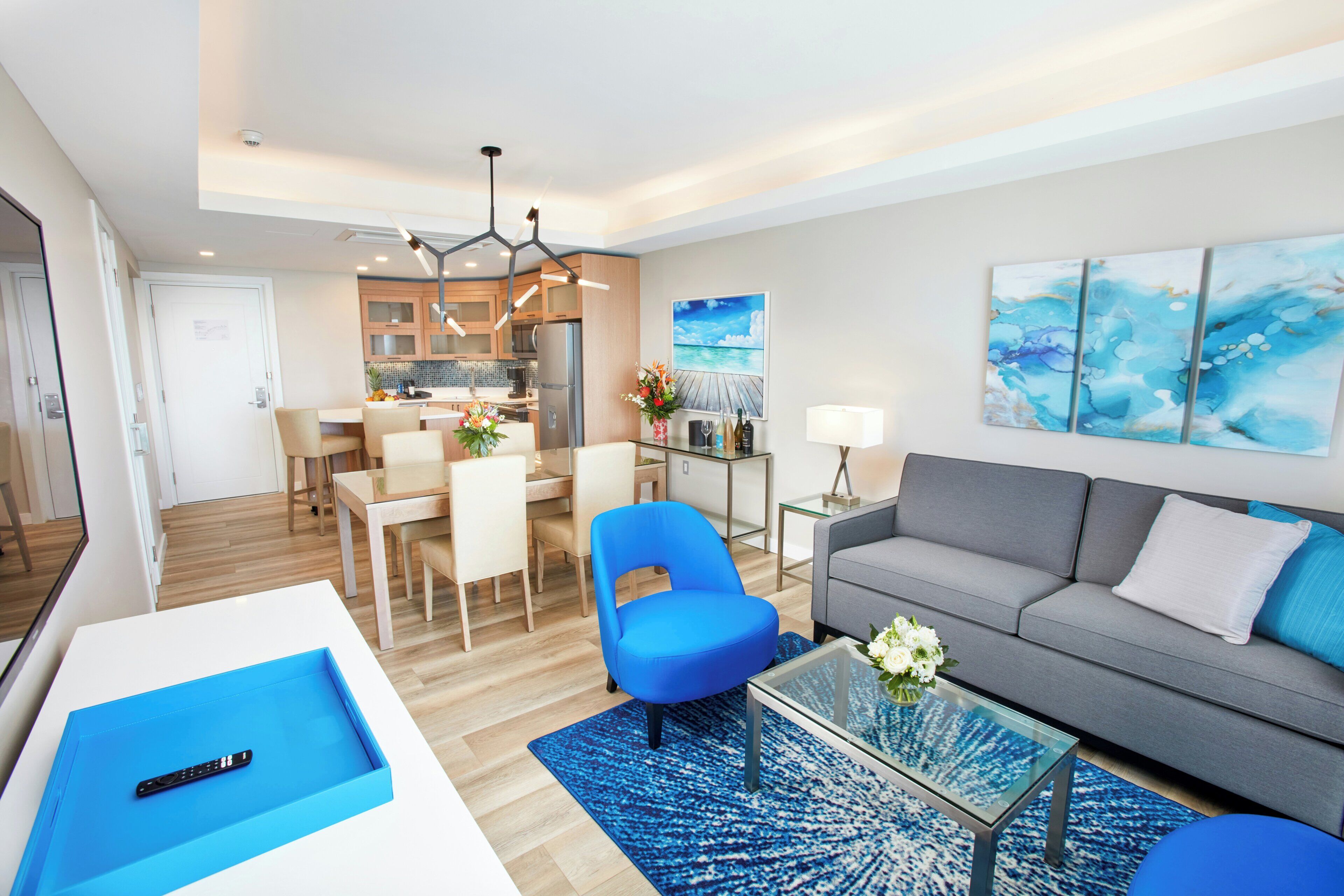 A modern living room with a sofa, a blue chair, a coffee table, and a dining area with chairs and a table.