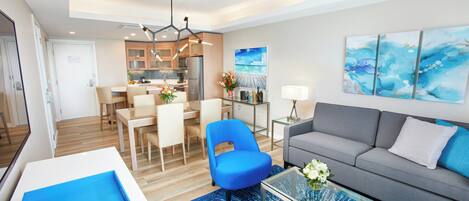 A modern living room with a sofa, a blue chair, a coffee table, and a dining area with chairs and a table.