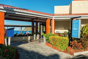 A covered outdoor area with a sign for SEA BREEZE restaurant & bar, outdoor seating with umbrellas, and a view of the sea.