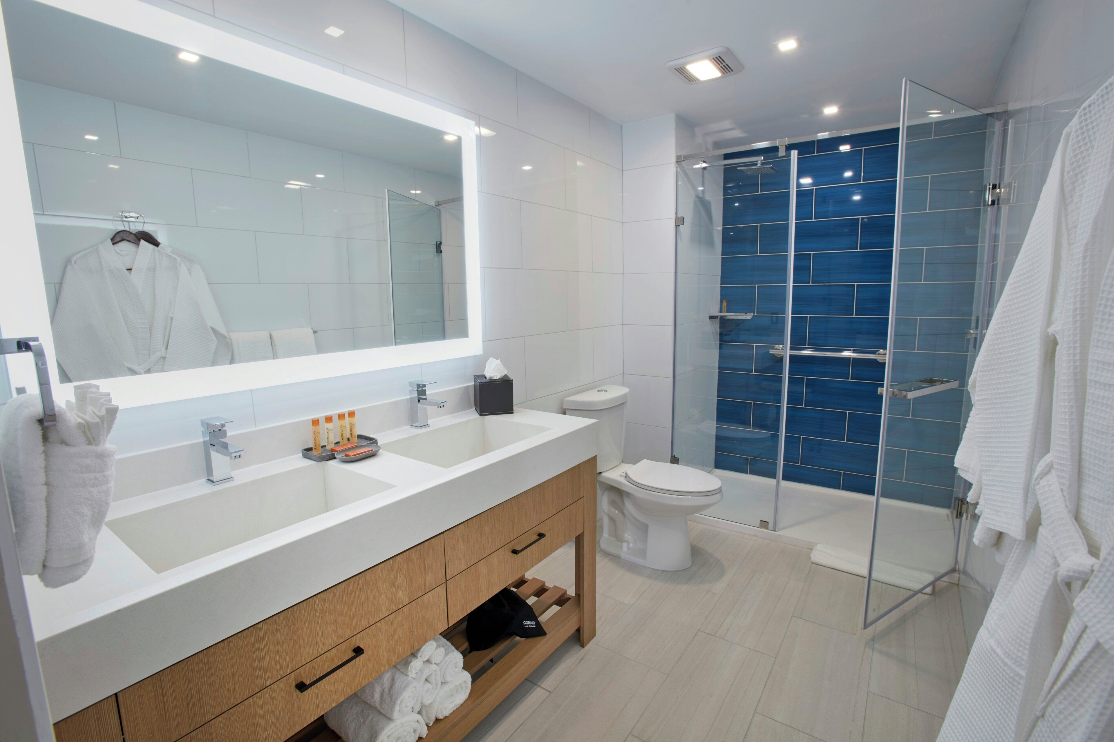 A modern bathroom with a large mirror, dual sinks, a toilet, and a glass-enclosed shower.