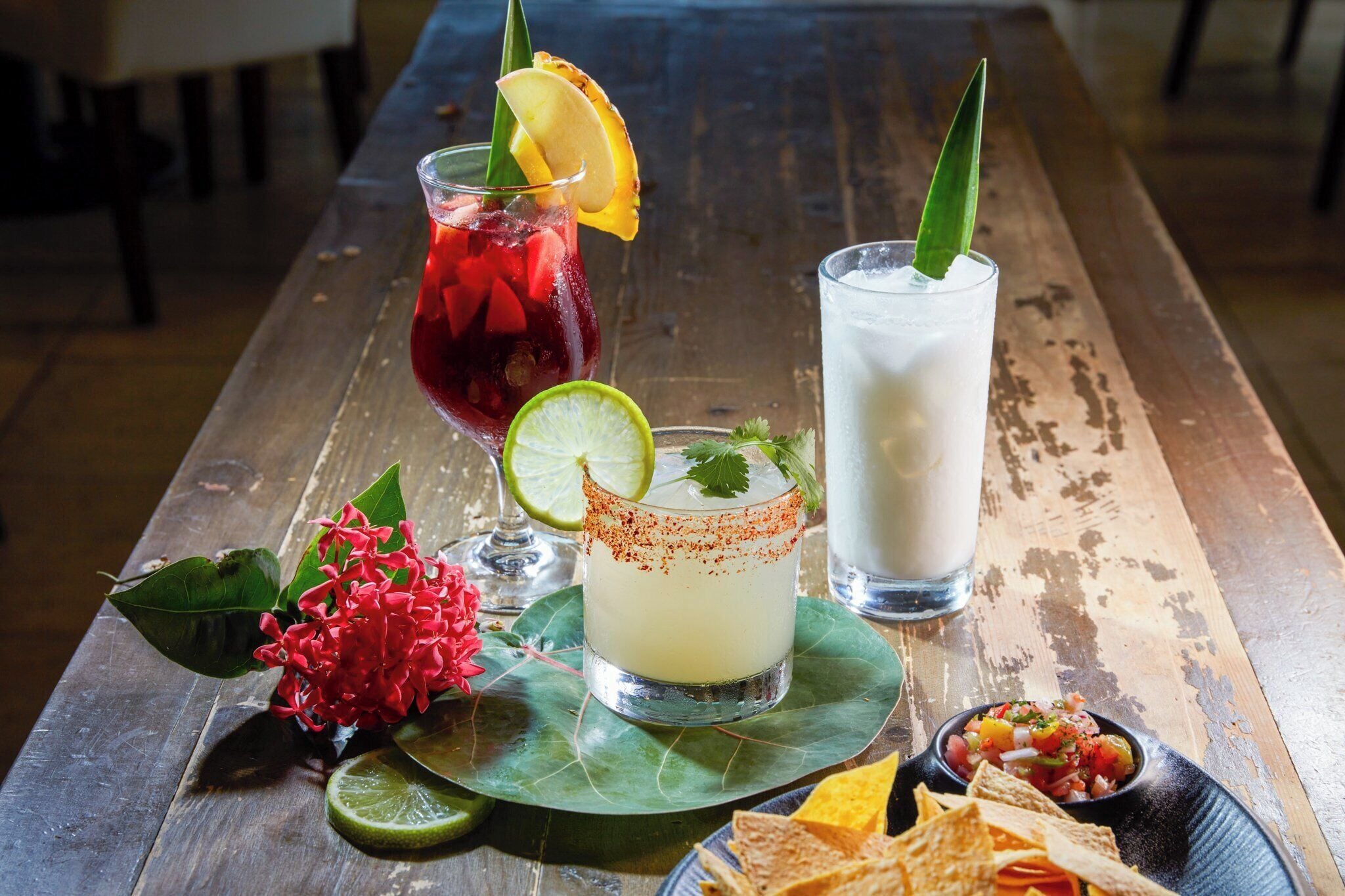 Une table en bois avec deux boissons, un quartier de citron vert et un petit bol de salsa.