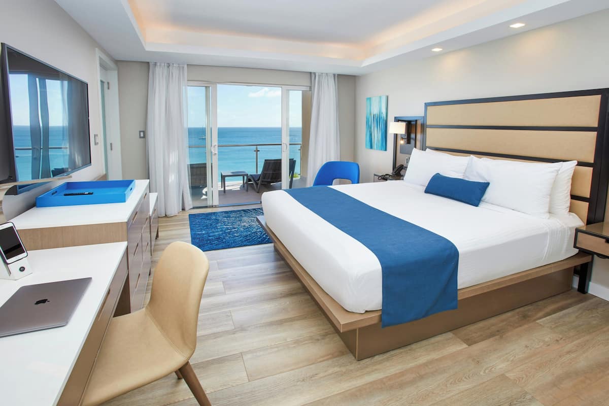 A hotel room with a bed, desk, chair, and a view of the ocean.