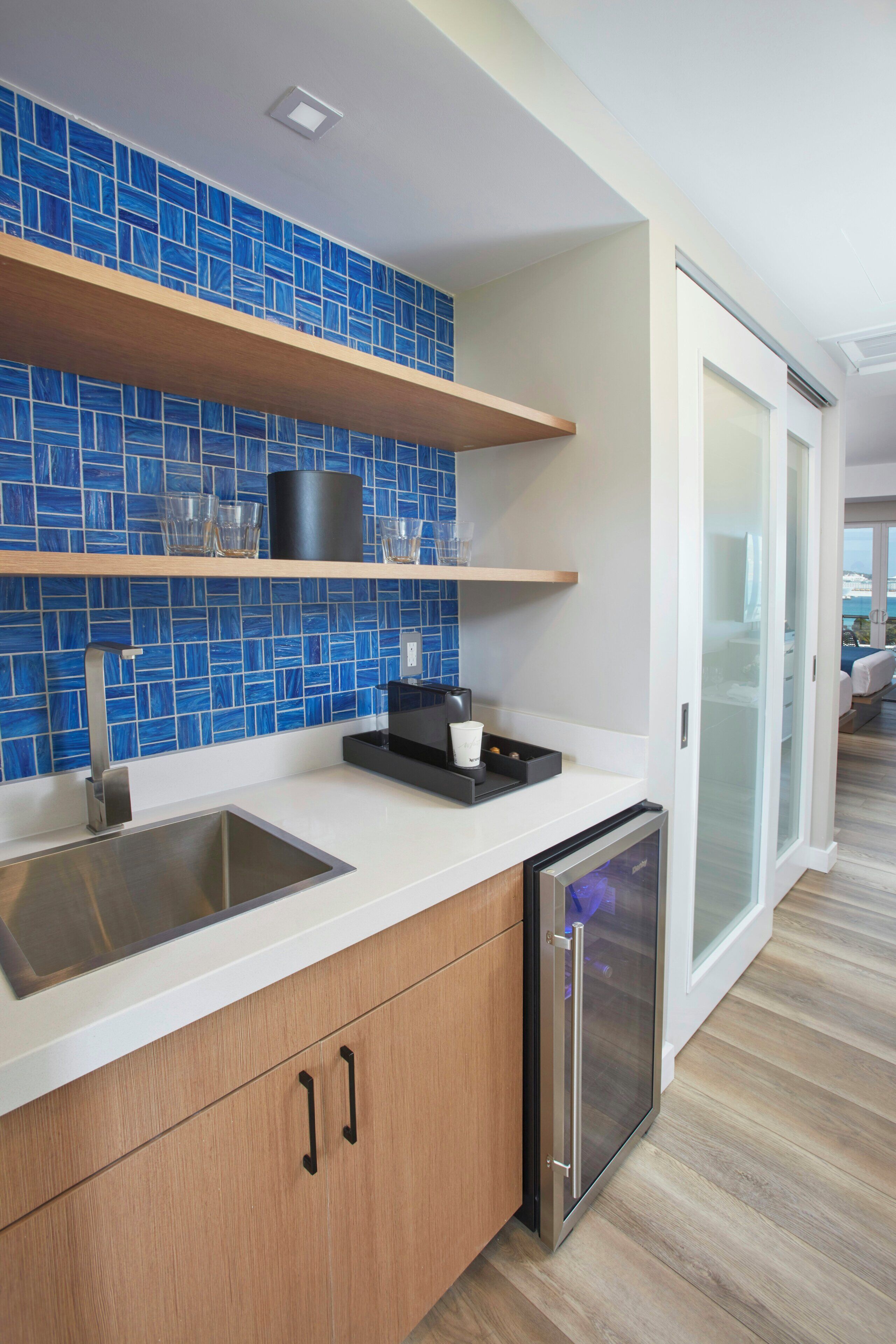 A modern kitchen with blue tiles, a dishwasher, and a countertop with a coffee maker.