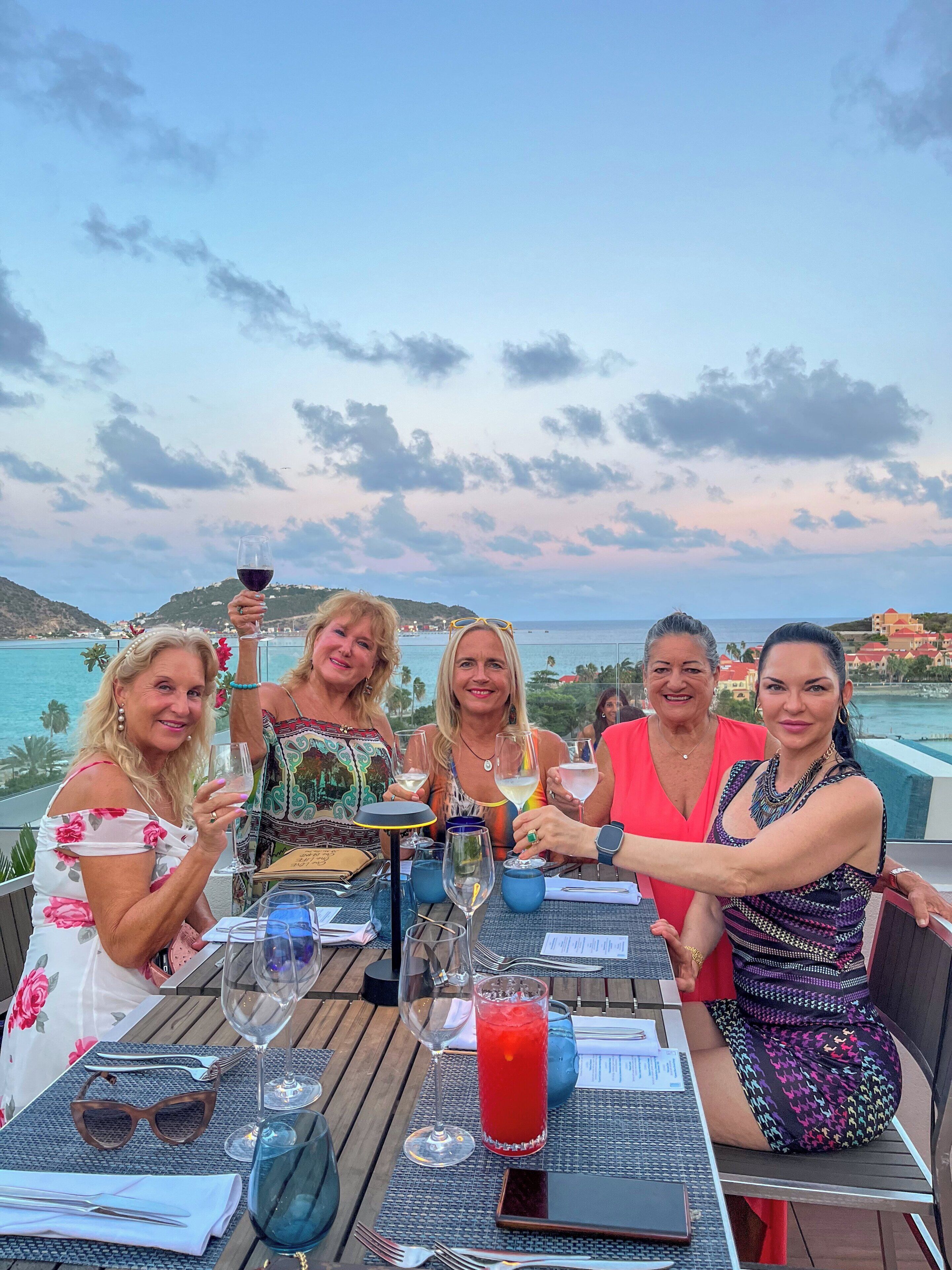 Un groupe de personnes est assis à une table à l'extérieur, devant des boissons, et profite d'une vue panoramique.