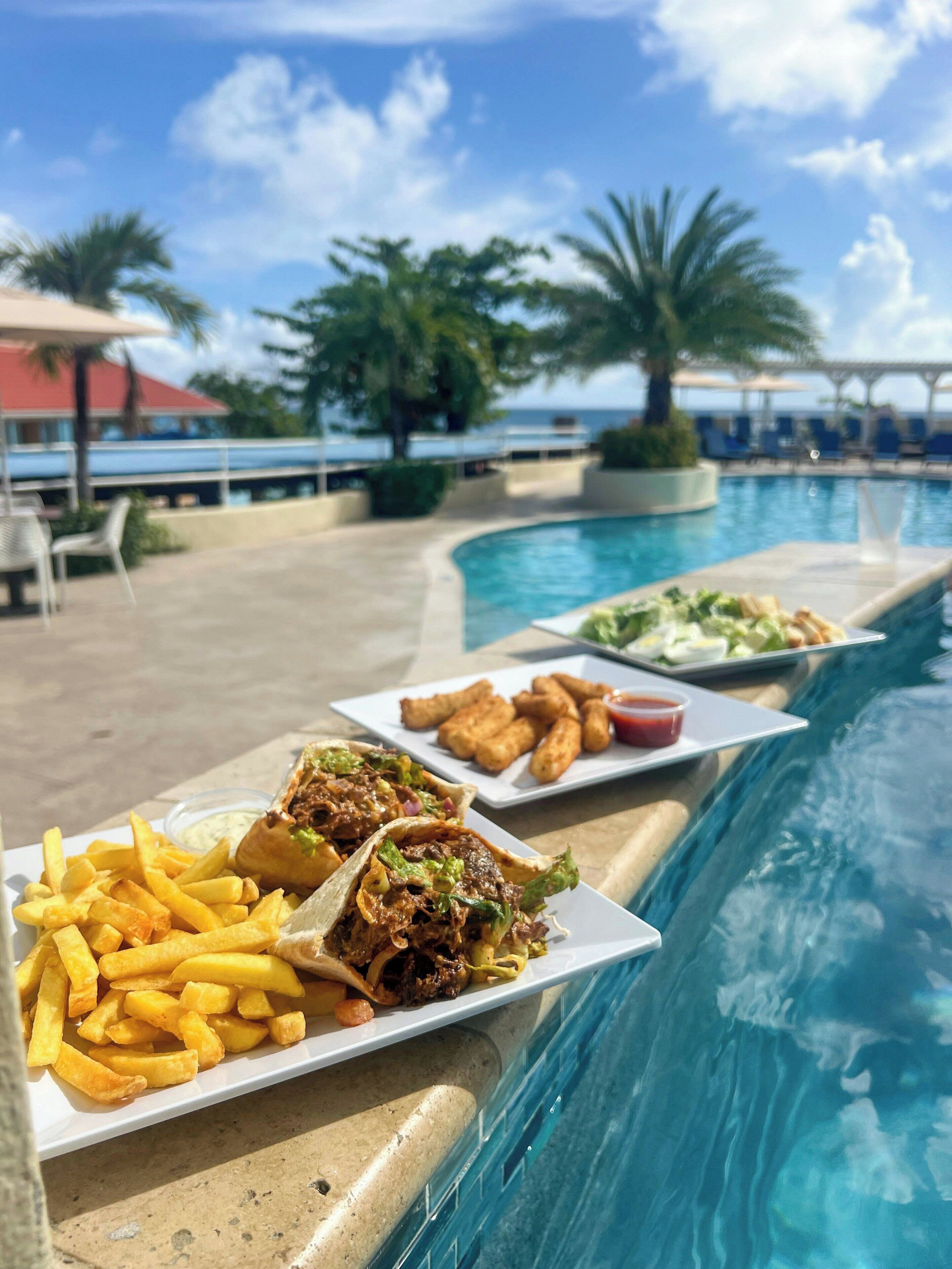 Ein Essbereich am Pool mit Blick auf den Ozean, mit einer Portion Pommes, einem Wrap und frittierten Speisen.