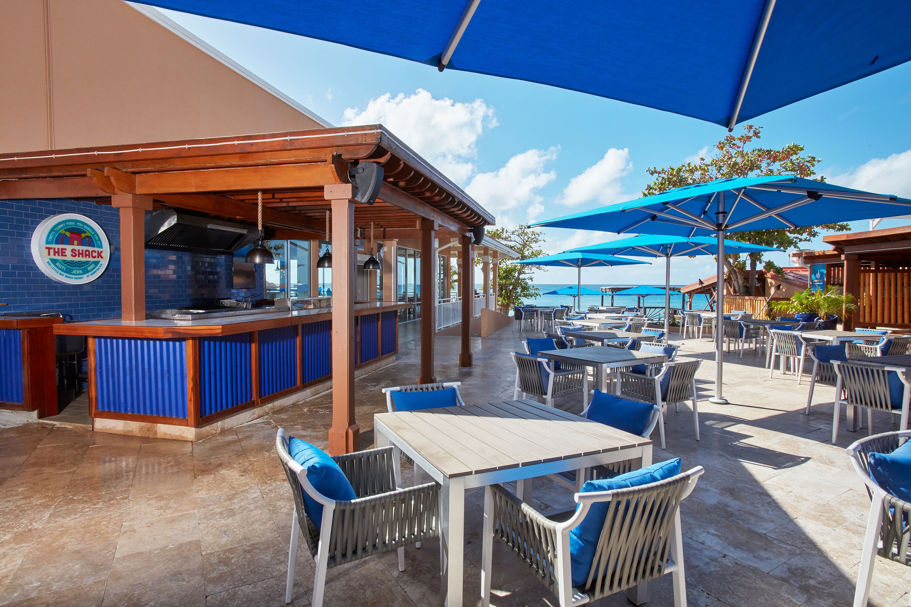 Een eethoek buiten met blauwe parasols, witte tafels en blauwe stoelen.
