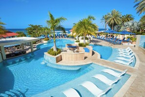 Un espace piscine avec des chaises longues, des palmiers et une vue sur l’océan.