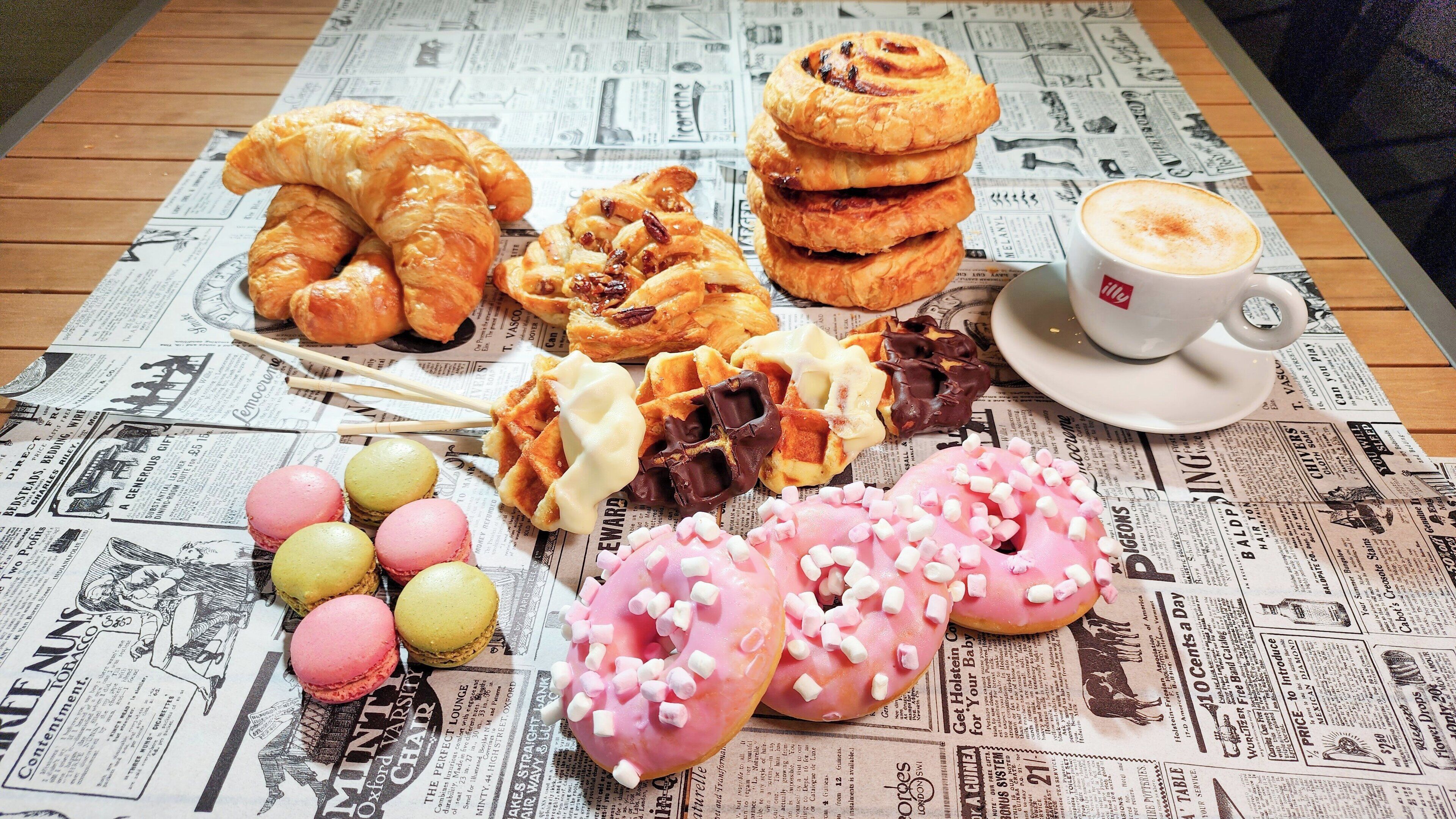 A variety of pastries and a cup of coffee on a newspaper-covered table.