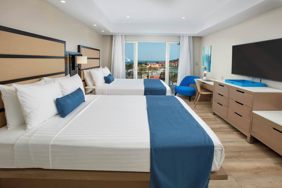 A hotel room with two beds, a desk, a TV, and a balcony with a view.