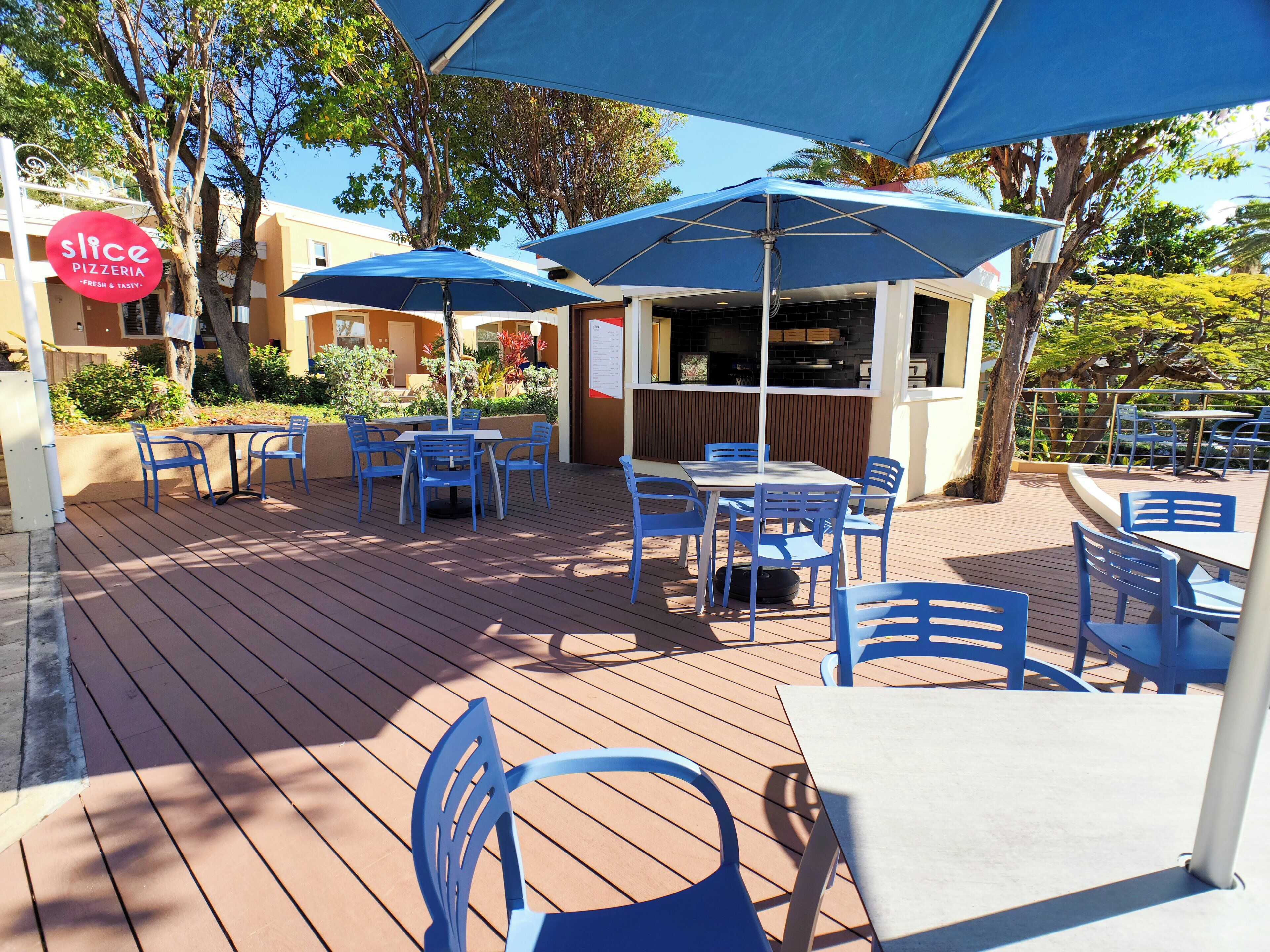 An outdoor patio with tables and chairs, umbrellas, and a pizza restaurant sign.