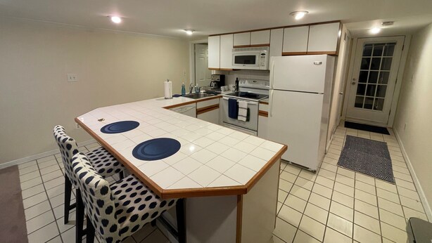 Cocina compacta con una isla central, electrodomésticos blancos y una silla estampada.