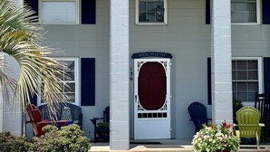 A two-story building with a red roof, white columns, and a dark red door. There are two green chairs and a potted plant in front. - The Sea Witch-Beautiful inlet views just one block from beach! (Murrells Inlet)