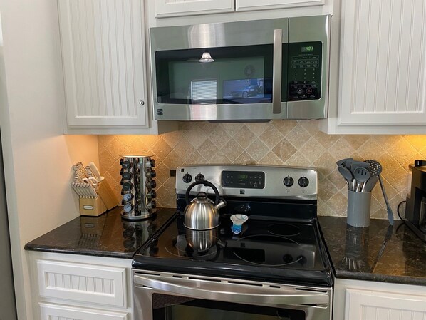 A kitchen with a stainless steel stove, microwave, and oven. There is a kettle on the stove, a knife block, and a utensil holder on the counter.