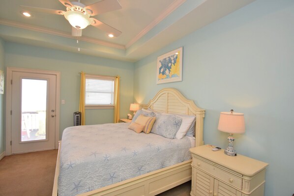 A bedroom with a bed, a nightstand, a lamp, a ceiling fan, and a door.