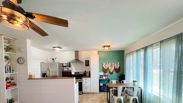 Een compacte keuken met een centraal eiland, een eethoek met een tafel en stoelen, en een plafondventilator.
