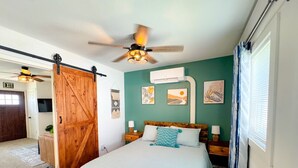 Een slaapkamer met een bed, een plafondventilator, een houten deur en kunst aan de muur.