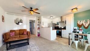 Een woonkamer met een bank, salontafel en een eethoek met stoelen. Achtergrond is een keuken.