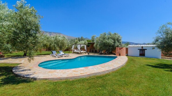 A swimming pool with a stone edge, surrounded by a grassy lawn and trees. - Cortijo Granadas Órgiva by Ruralidays (Granada)