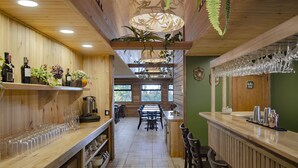 A wooden interior with a bar area, shelves with bottles, and hanging plants. - Das Dorf (Pucón)