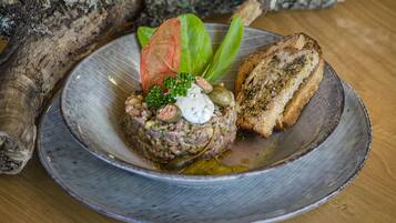 Un plato de tártara de ternera con pan tostado, adornado con una hoja y una cucharada de salsa.