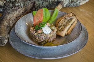 Un plato de tártara de ternera con pan tostado, adornado con una hoja y una cucharada de salsa.
