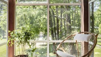 Una habitación con paneles de madera, ventanas amplias, una silla de mimbre y plantas en macetas.