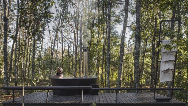 A wooden deck with a hot tub and a hanging towel rack in a forested area. - Das Dorf (Pucón)