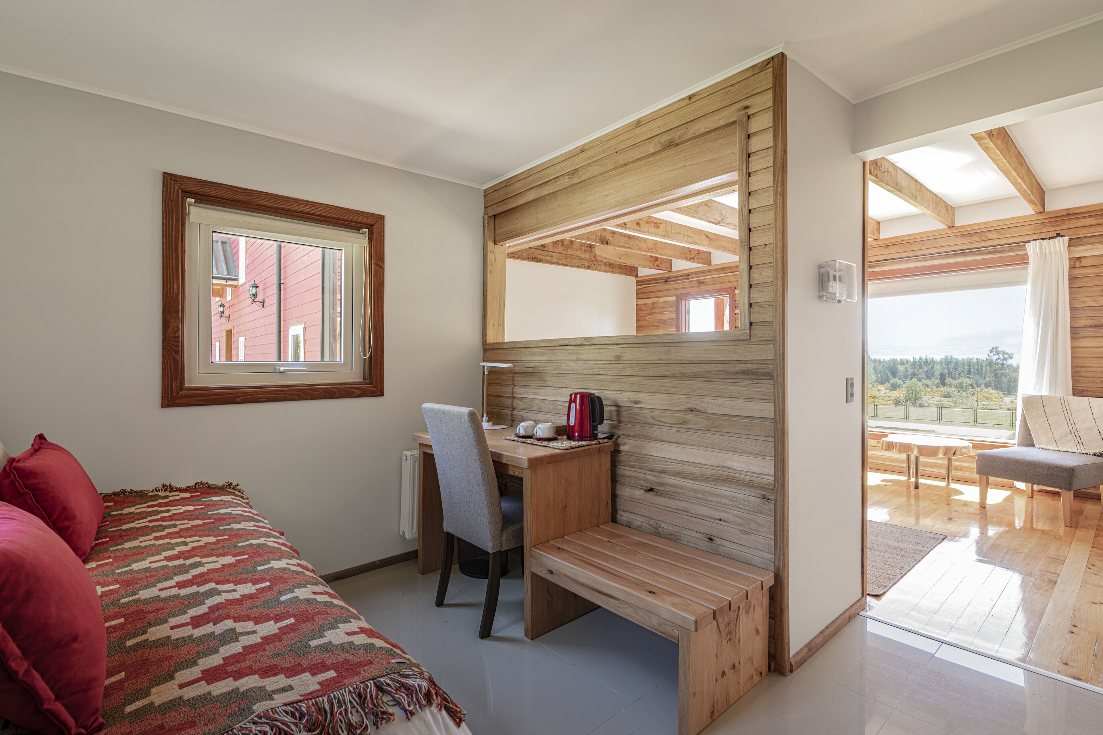A bedroom with a bed, a desk, and a view of the outdoors.