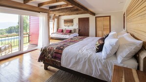 A spacious bedroom with a large bed, wooden beams, a balcony with a view, and a sliding door leading to another room. - Das Dorf (Pucón)
