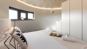 Un dormitorio moderno con una cama grande, una mesita de noche con lámpara, una ventana y un armario.
