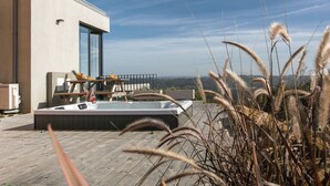 Un área moderna de hidromasaje al aire libre con un deck de madera, un ventanal y vistas al paisaje.