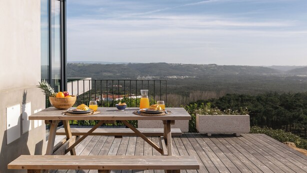 Terraza de madera con una mesa preparada para el desayuno, con vistas a un paisaje pintoresco.
