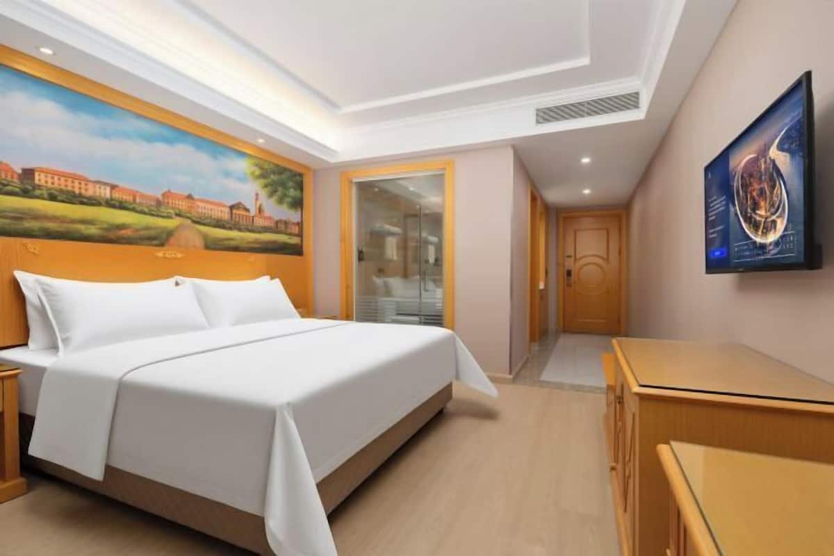 Una habitación de hotel con cama, escritorio, un cuadro en la pared y televisor.