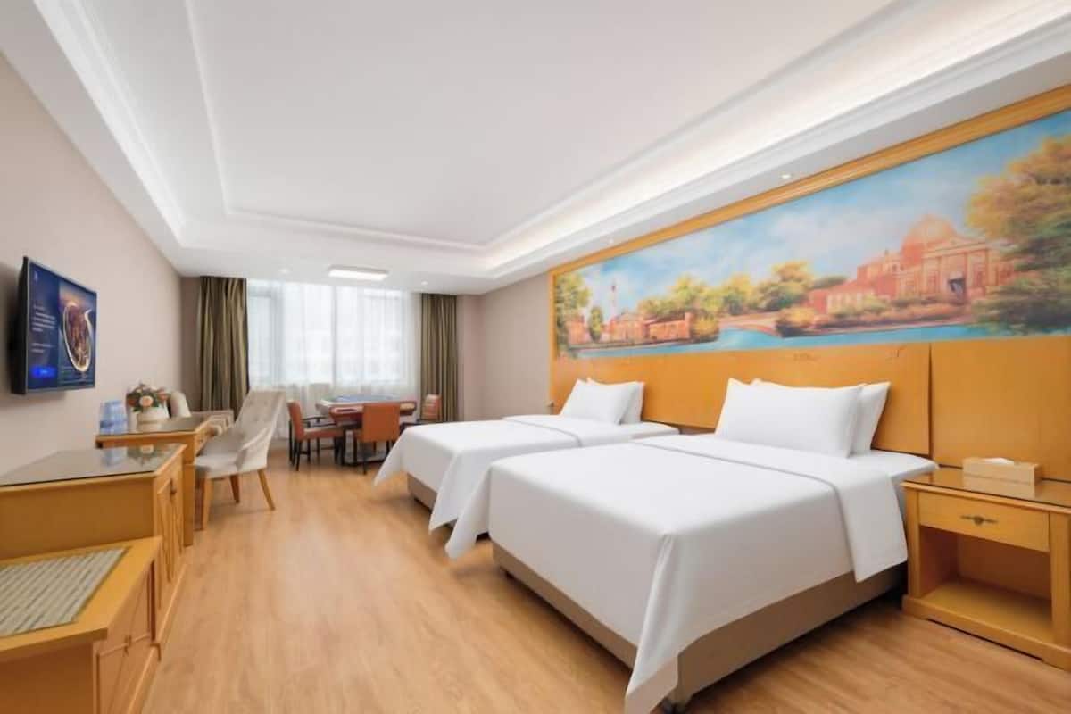 Una habitación de hotel con dos camas, un escritorio, una silla y un cuadro en la pared.