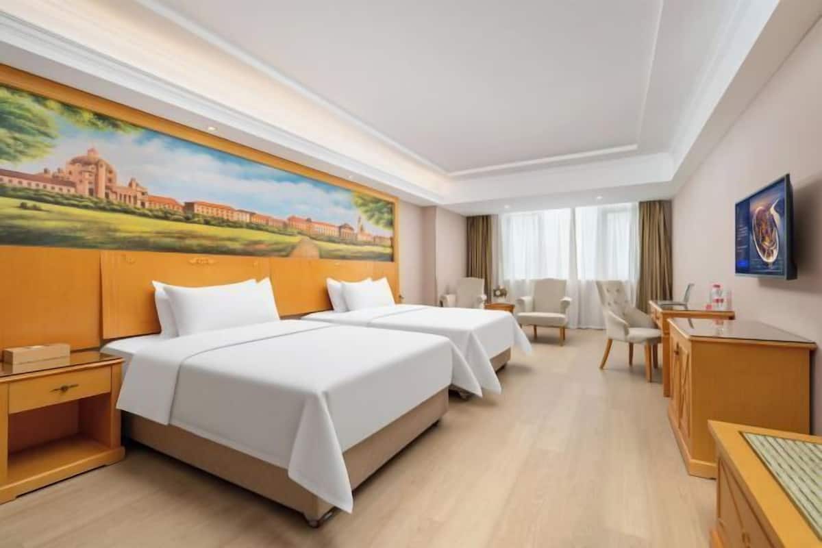 Habitación de hotel con dos camas, un escritorio, una silla y un cuadro en la pared.