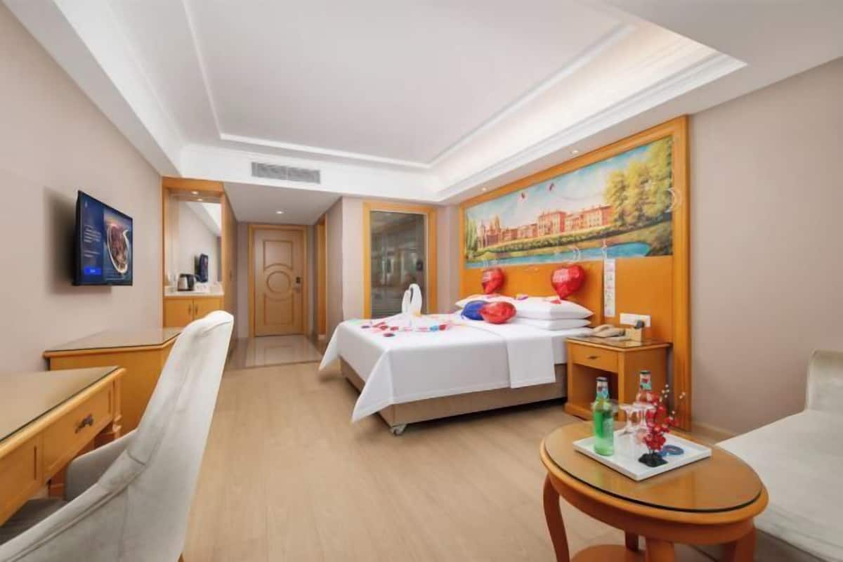 Habitación de hotel con cama, escritorio, silla, mesita, un cuadro en la pared y televisor.