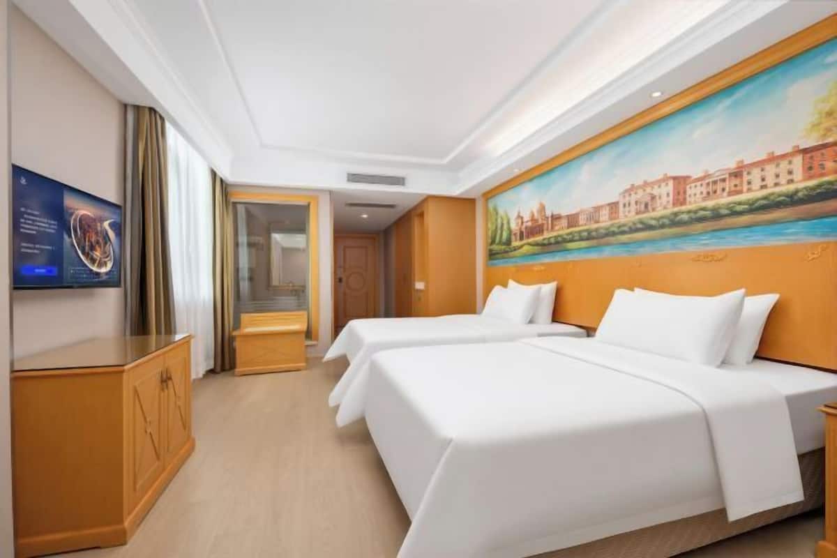 Una habitación de hotel con dos camas, un televisor, un cuadro en la pared y un armario de madera.