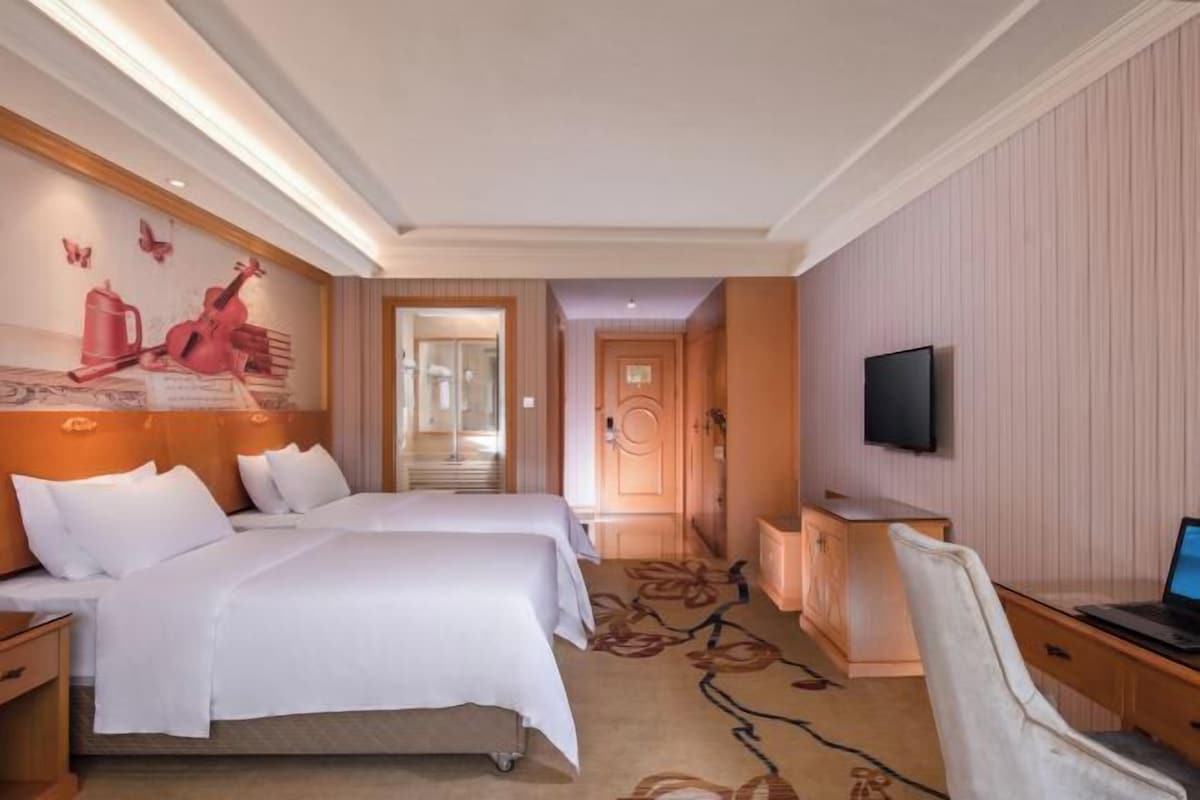 A hotel room with two beds, a desk with a computer, a television, and a shower area.